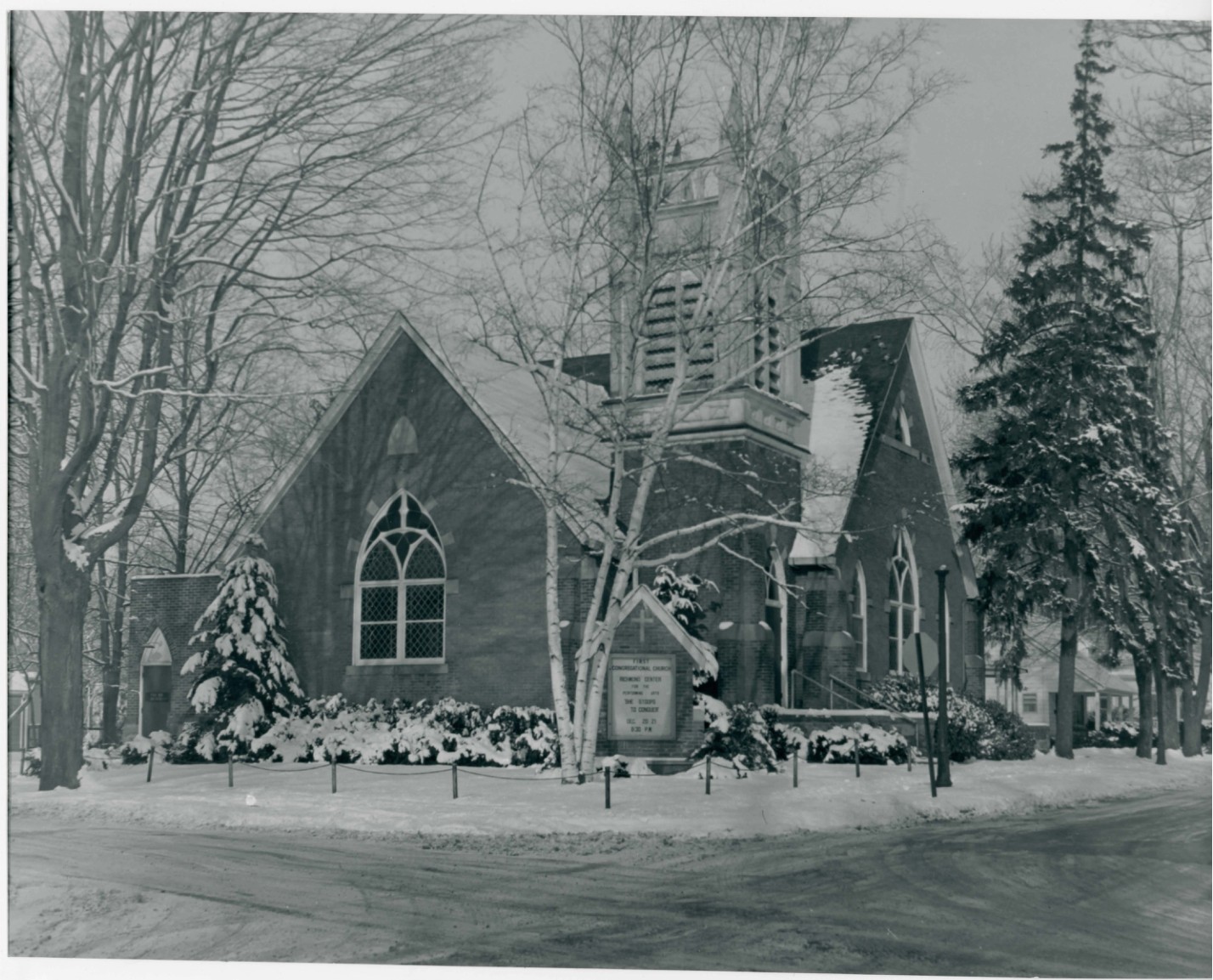 Photograph of a church in winter with snow on the ground and trees.